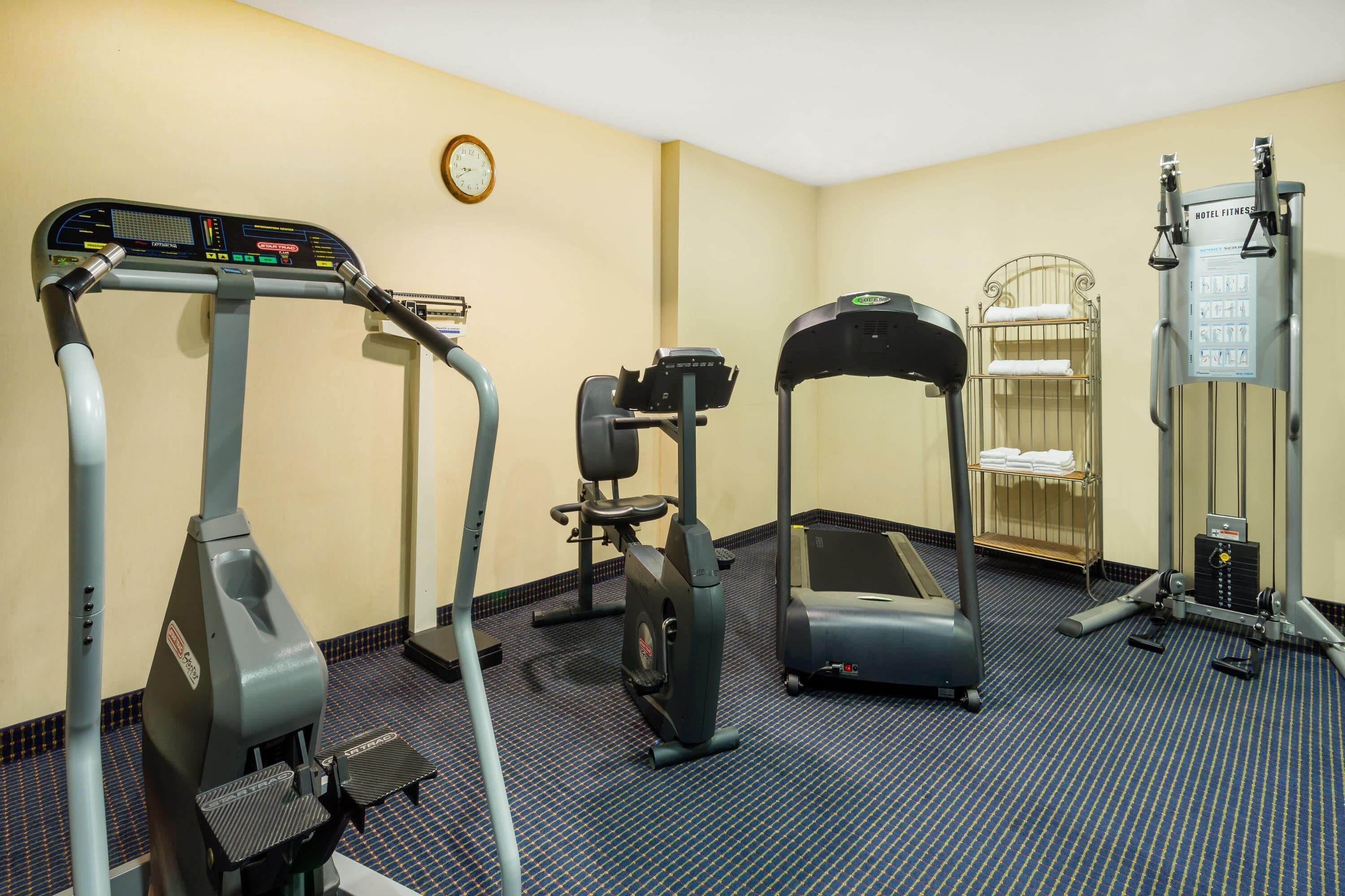 A hotel fitness center with cardio machines, a weight bench, and a wall-mounted scale.
