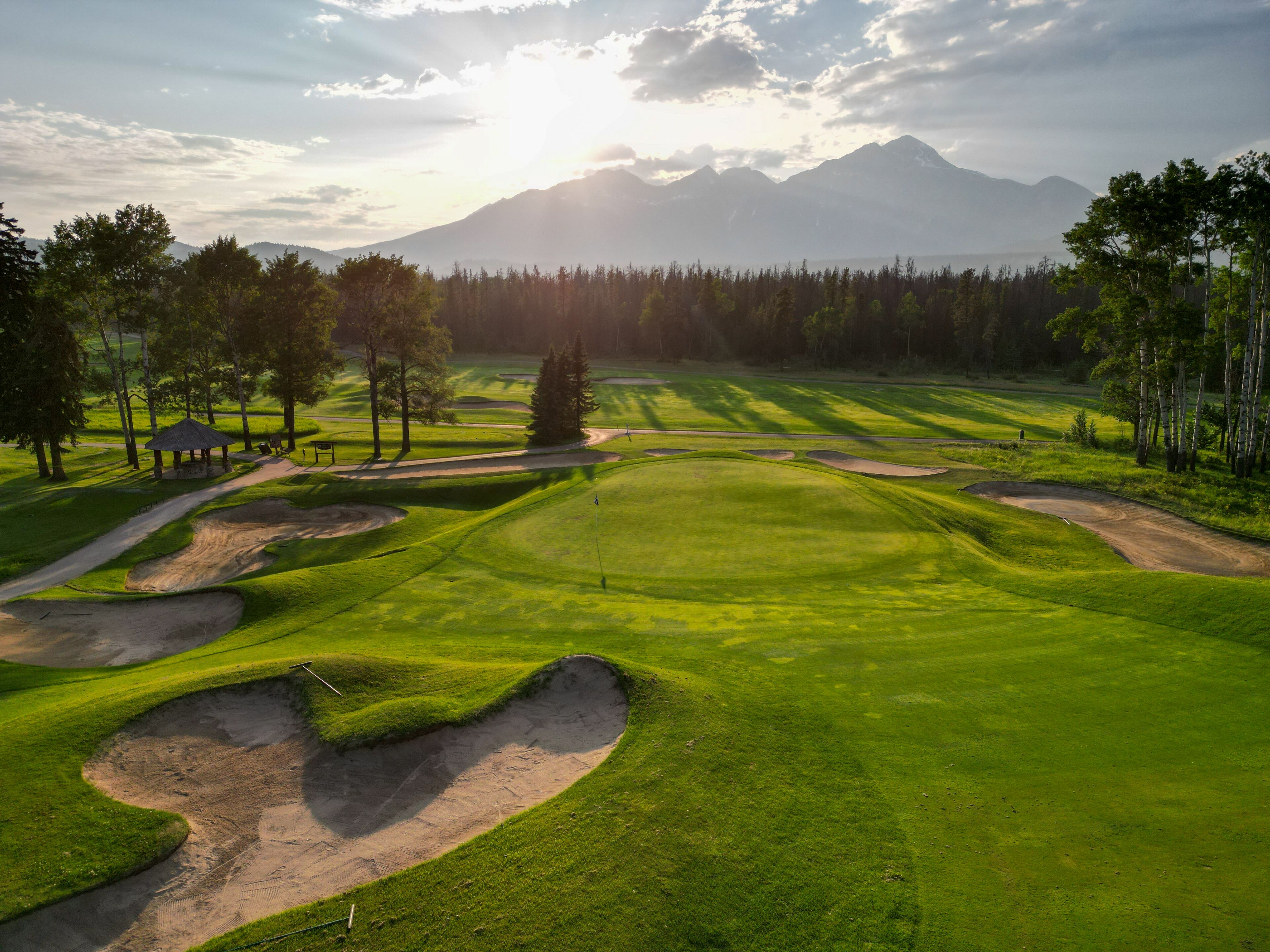 Un campo de golf con búnkeres, un pabellón y una montaña al fondo.