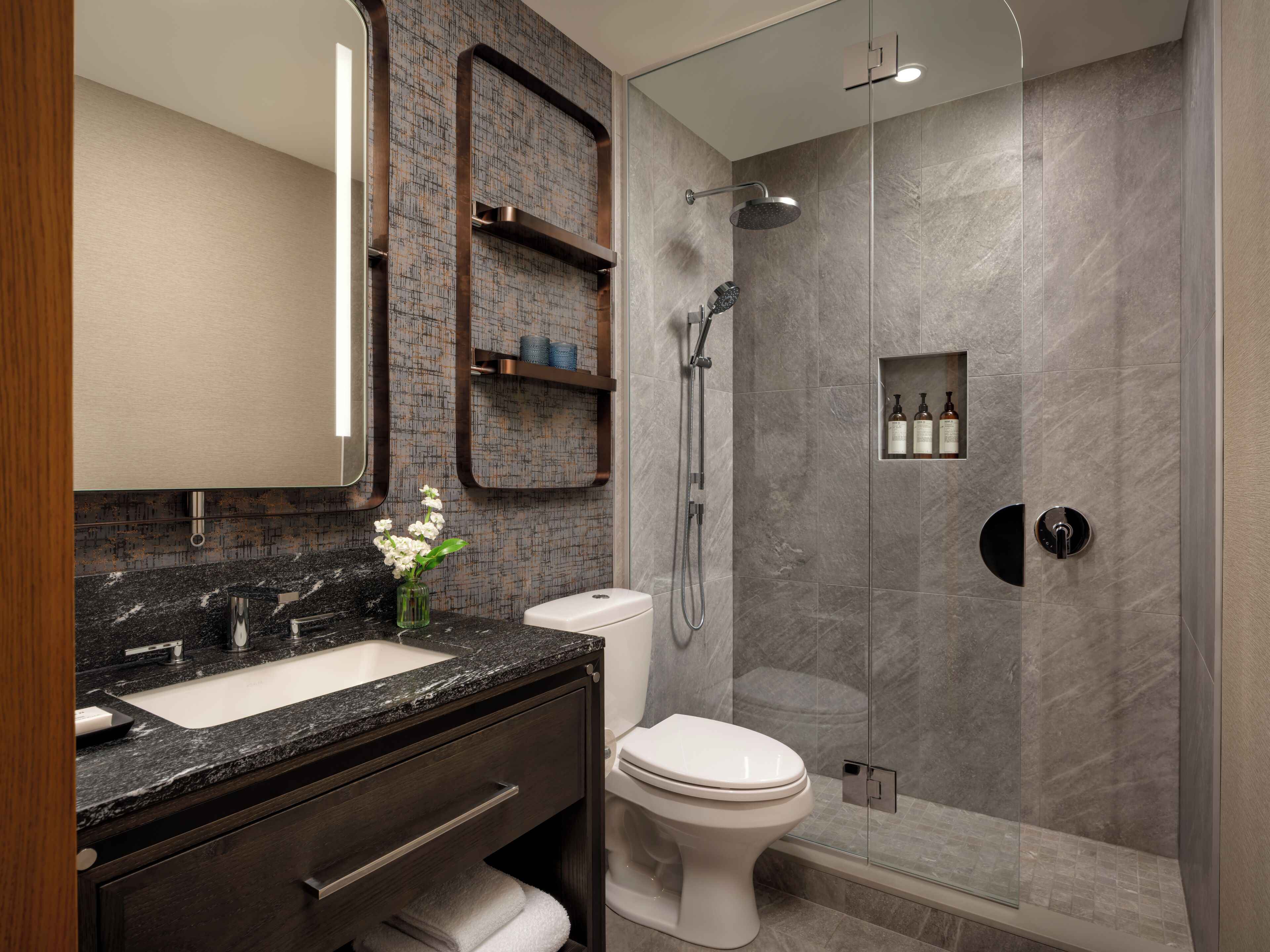 A modern bathroom with a marble sink, dark wooden vanity, a white toilet, and a glass-enclosed shower area.