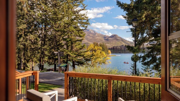 A balcony with two chairs, a wooden railing, and a view of a lake with mountains in the background. - Fairmont Jasper Park Lodge (Jasper)