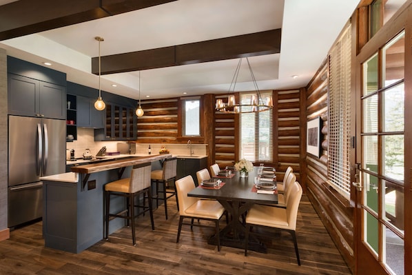 Una cocina moderna con una isla central, asientos tipo bar y una zona de comedor con una mesa grande y sillas.