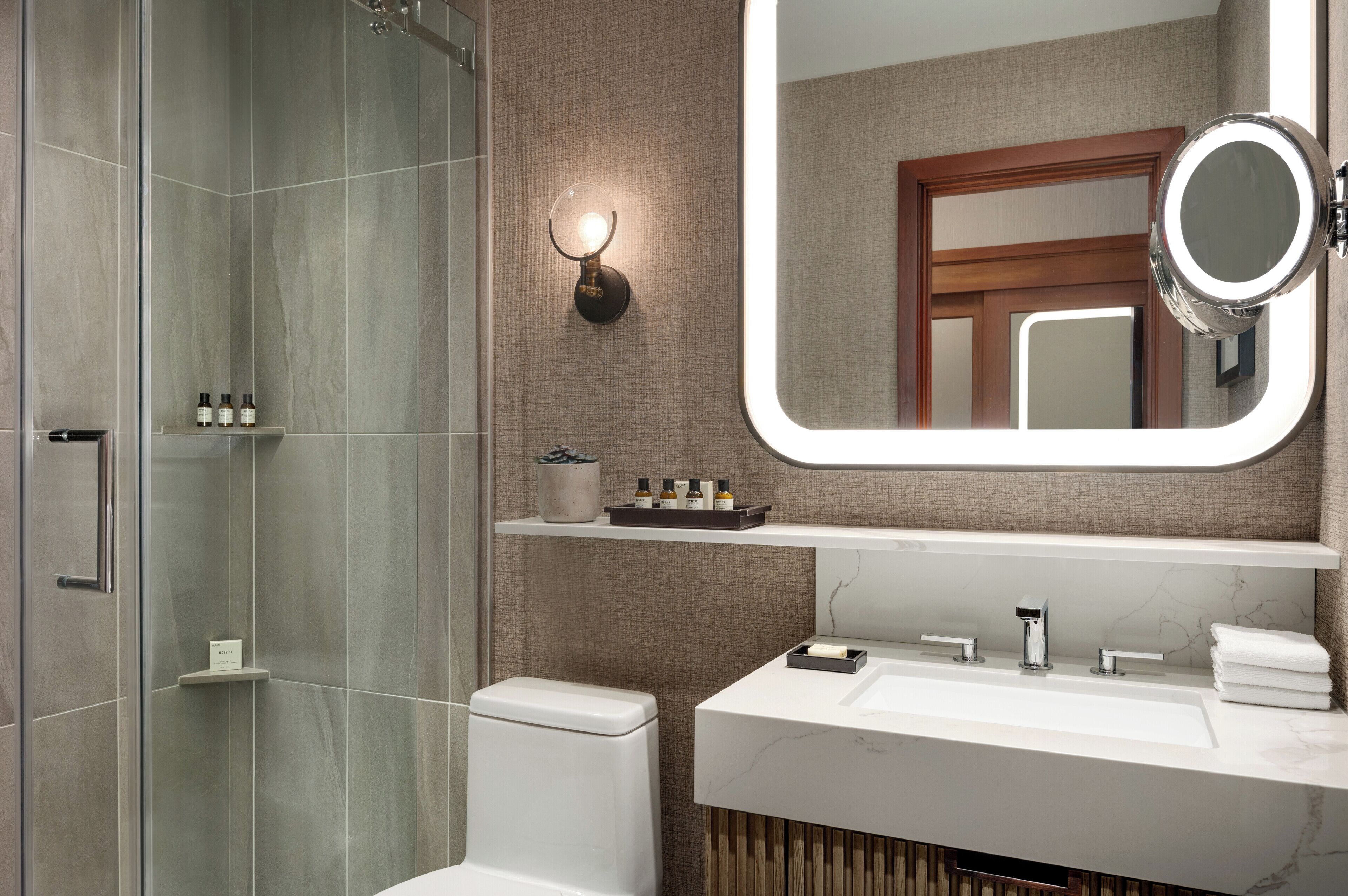 Un baño moderno con ducha de vidrio, tocador con espejo grande y un inodoro.