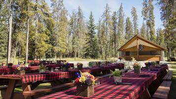 An outdoor dining area with red and black checkered tables, surrounded by tall trees.