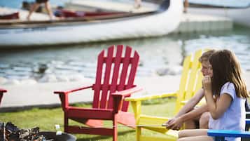 A person roasting marshmallows over a fire pit with red and yellow Adirondack chairs nearby.