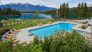 A pool area with lounge chairs, a flag, and a view of a lake and mountains. - Fairmont Jasper Park Lodge (Jasper)