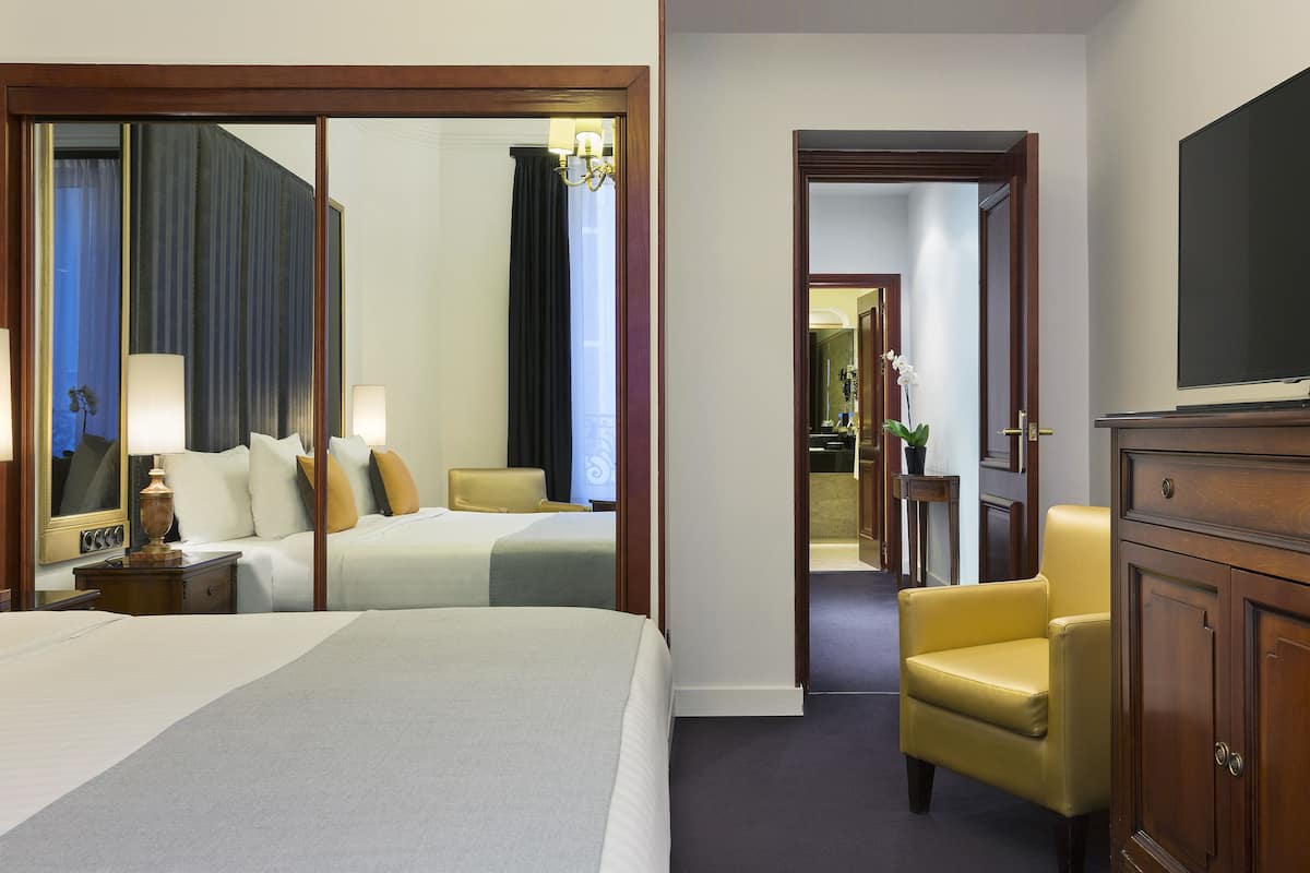 A hotel room with two beds, a sitting area with a chair, a television, and a mirror.