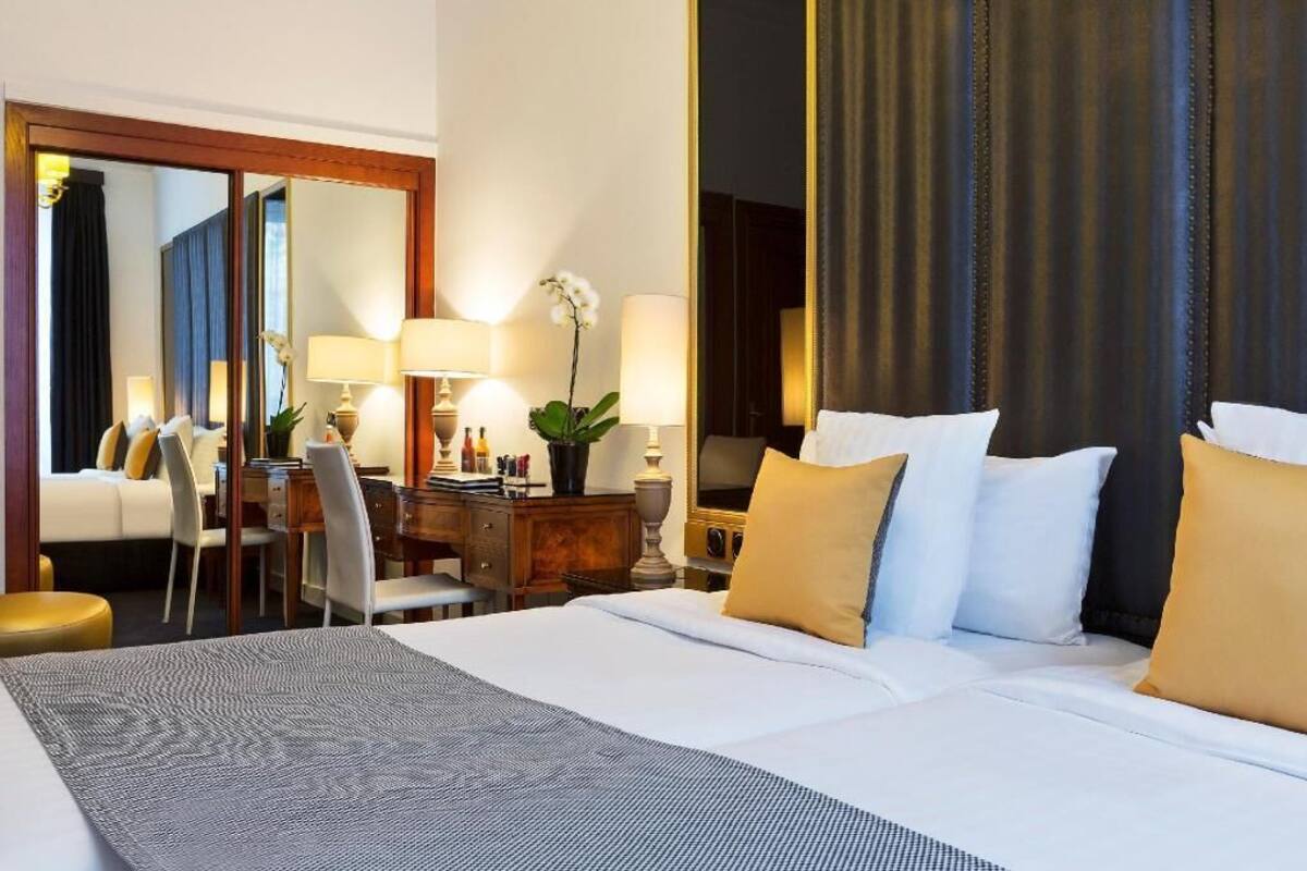 A hotel room with a large bed, a desk with a chair, a mirror, and a plant.