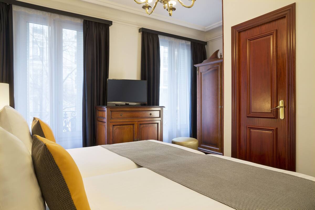A hotel room with a bed, a television on a wooden cabinet, a wardrobe, and a door.