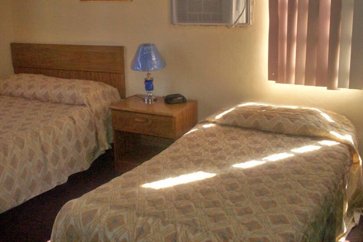 Ein Zimmer mit zwei Betten, einem Nachttisch mit Lampe und einem Fenster mit Jalousien.