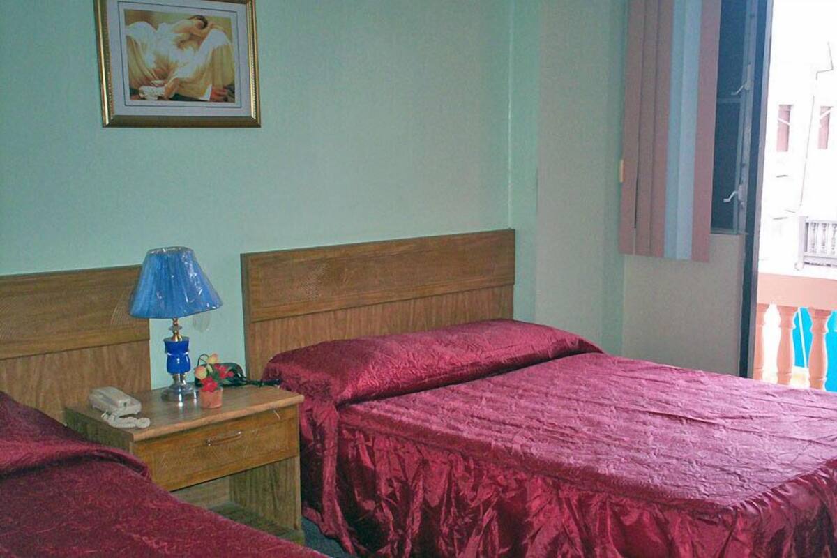 Ein Hotelzimmer mit zwei Betten, einem Holz-Kopfstück, einem Nachttisch mit Lampe, einem Telefon und einem gerahmten Bild an der Wand.