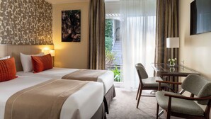 A hotel room with two beds, a desk with a chair, a TV, and a balcony with curtains. - Les Jardins d'Eiffel (Paris)