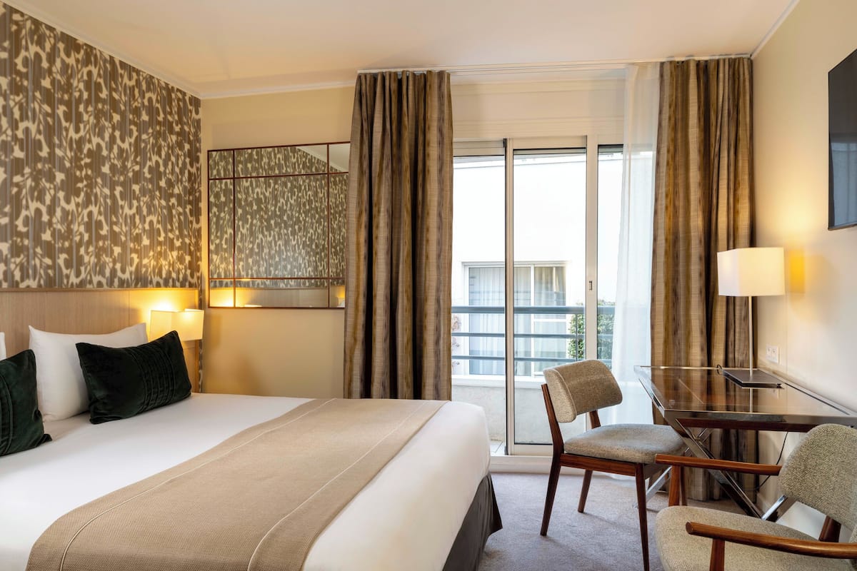 Ein Hotelzimmer mit einem großen Bett, einem Schreibtisch mit Stuhl und Blick ins Freie durch eine Schiebetür.
