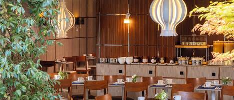 Un restaurante con paneles de madera, lámparas colgantes y mesas dispuestas con platos y tazas blancos.