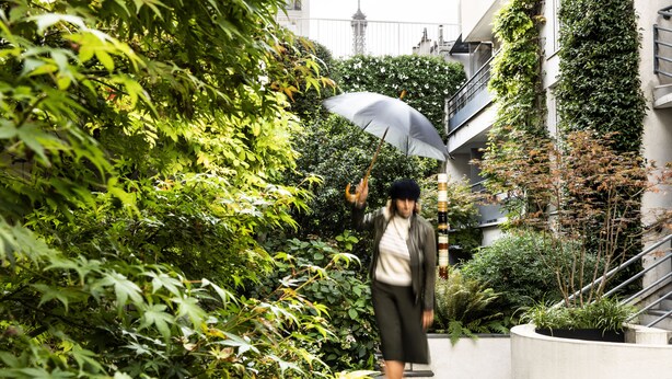 A person walking on a pathway surrounded by lush greenery and a staircase. - Les Jardins d'Eiffel (Paris)