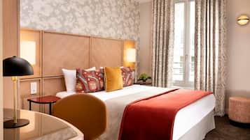 Quarto de hotel com cama, escrivaninha, cadeira, luminária e janela com cortinas.