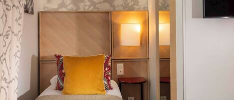 Une chambre d’hôtel avec un lit, une table de chevet, un miroir et une lampe fixée au mur.