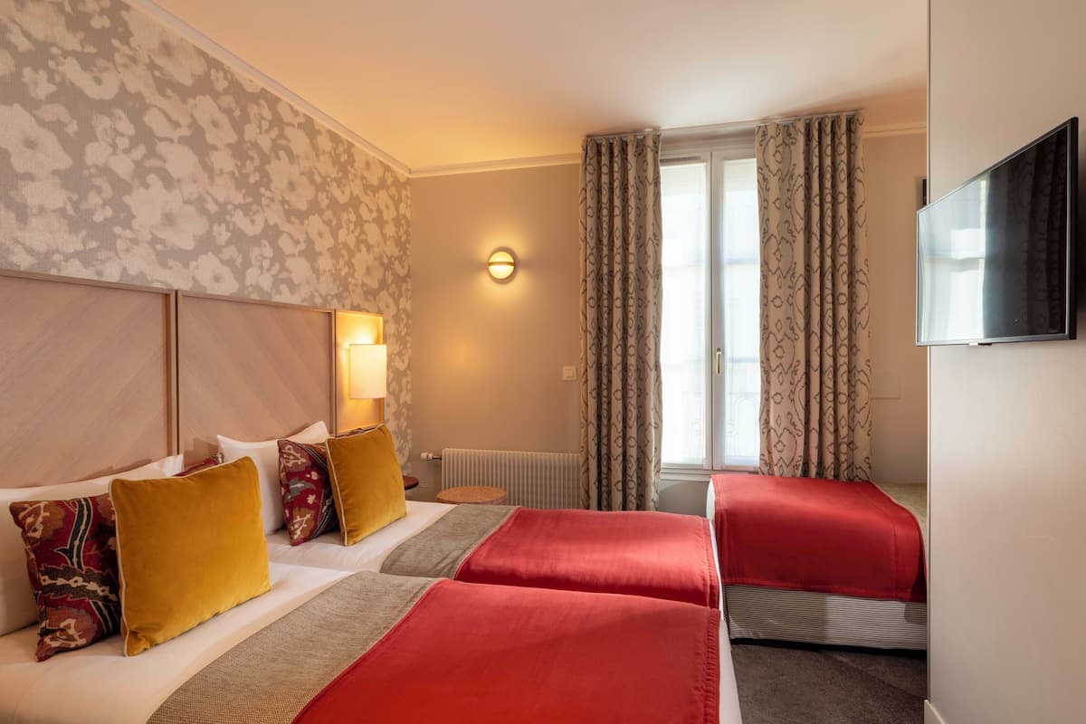 Ein Hotelzimmer mit zwei Betten, einem Fernseher, einer Lampe und einem Fenster mit Vorhängen.