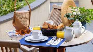 Disposição para o pequeno-almoço com croissants, sumo de laranja e uma cesta de vime sobre uma mesa ao ar livre.