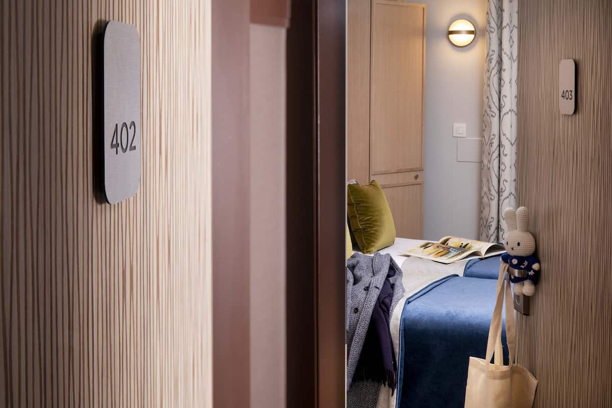 Ein Hotelzimmer mit Bett, Nachttisch, Lampe, Teddybär und einer Zimmernummer.