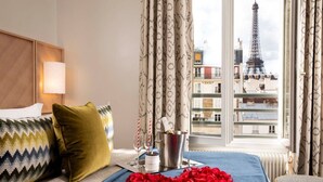 A hotel room with a bed, a nightstand, a bottle of champagne, and a bucket with a bottle. - Les Jardins d'Eiffel (Paris)