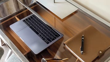Uma mesa de vidro com um laptop, uma caneta e óculos.