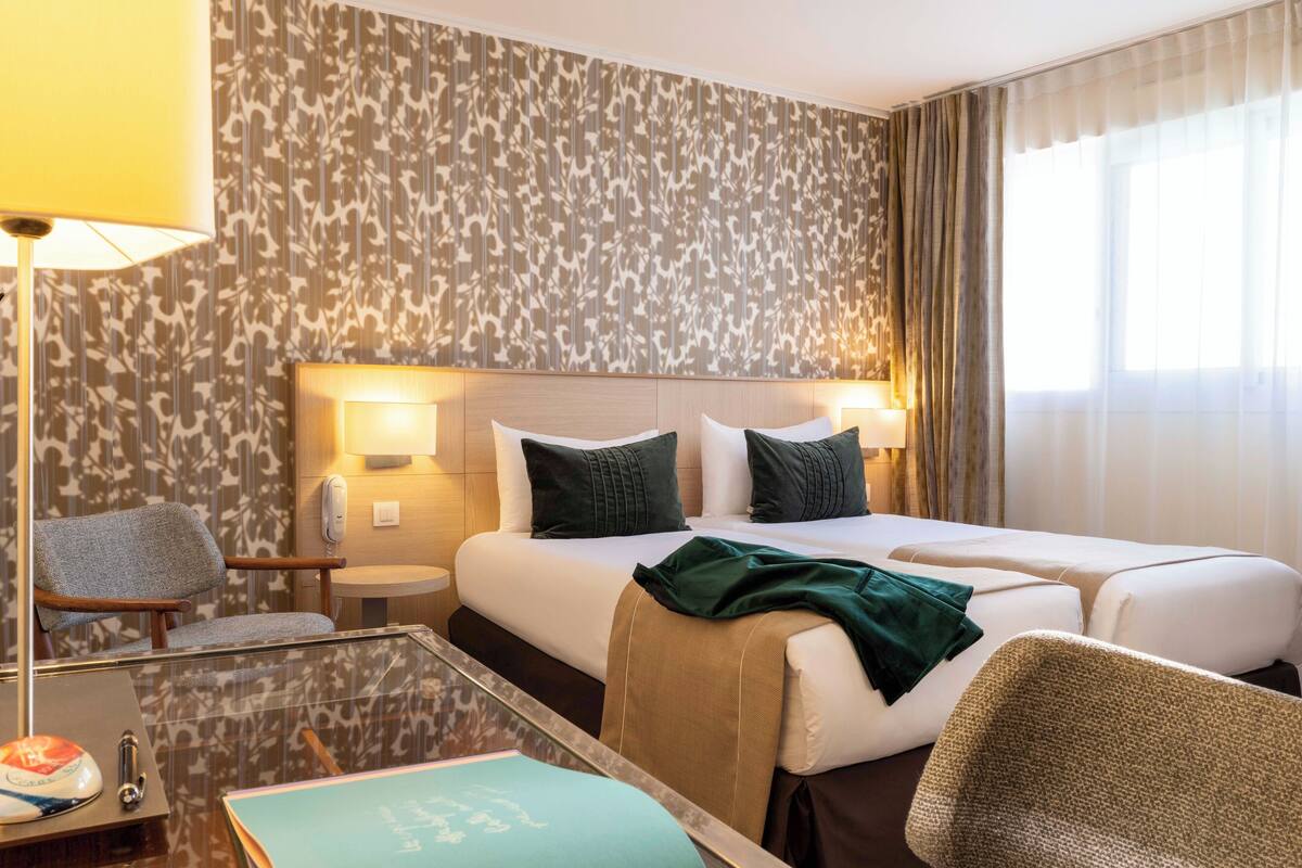 Ein Hotelzimmer mit zwei Betten, einer Sitzecke mit einem Sessel, einem kleinen Tisch und einer Lampe.