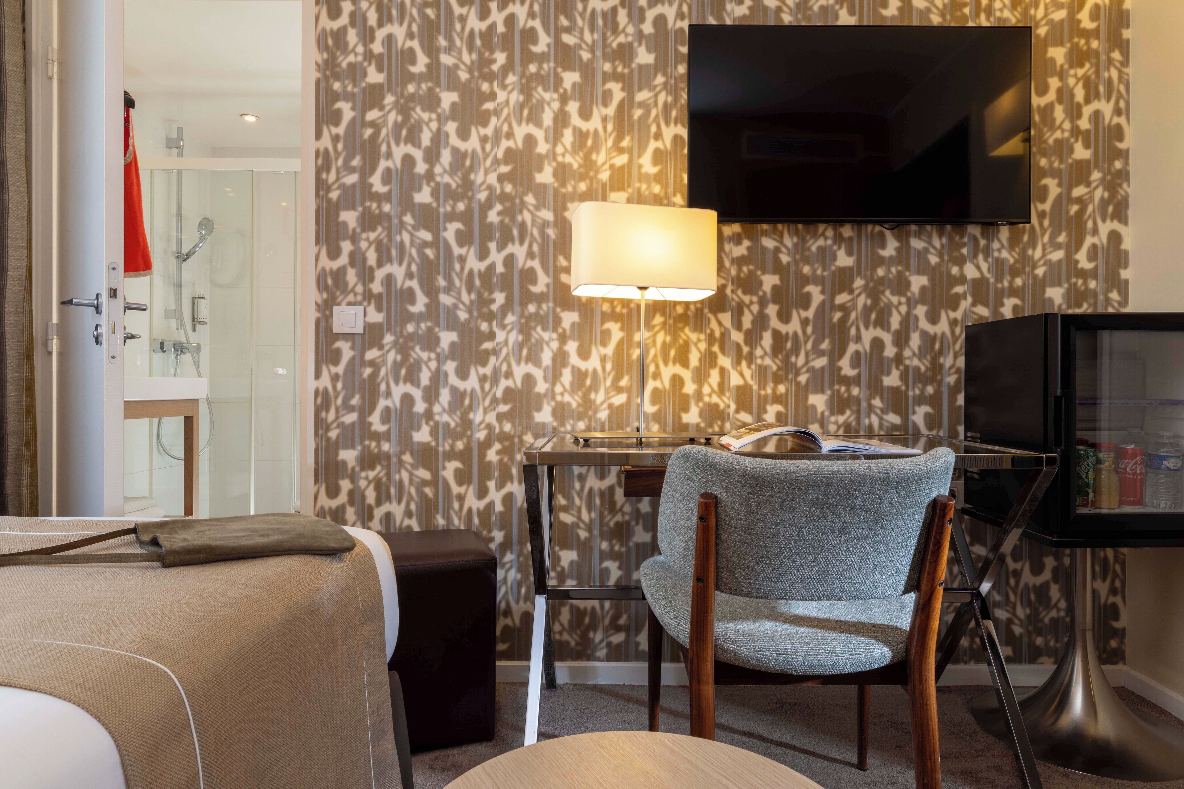 Une chambre d’hôtel comprenant un lit, un bureau avec une lampe, une chaise, une télévision et un espace douche.