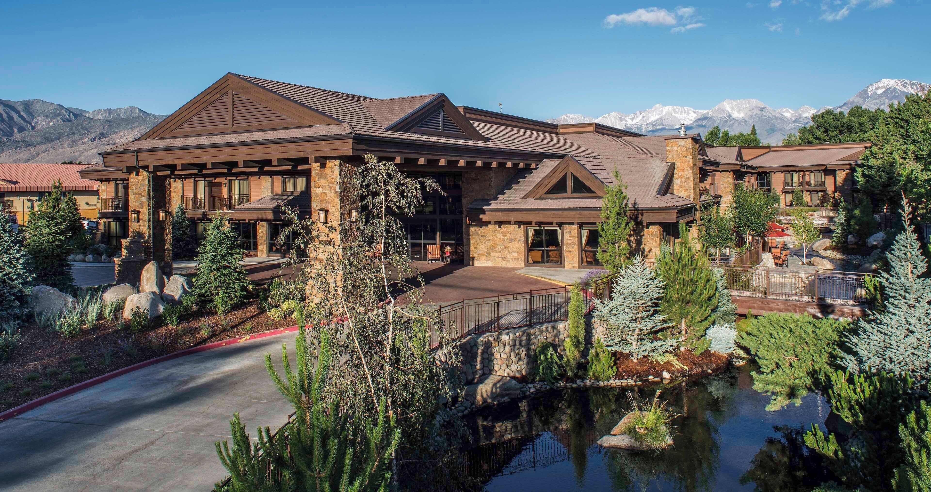 A large, multi-story lodge with a stone facade, multiple balconies, and a view of snow-capped mountains.