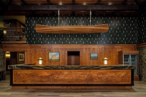 A reception desk with a wooden finish, two wall-mounted lamps, and a framed painting above the door. - Wayfinder Bishop (Bishop)