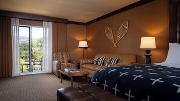 A hotel room with a bed, a sofa, a chair, a coffee table, and a view of the outdoors.