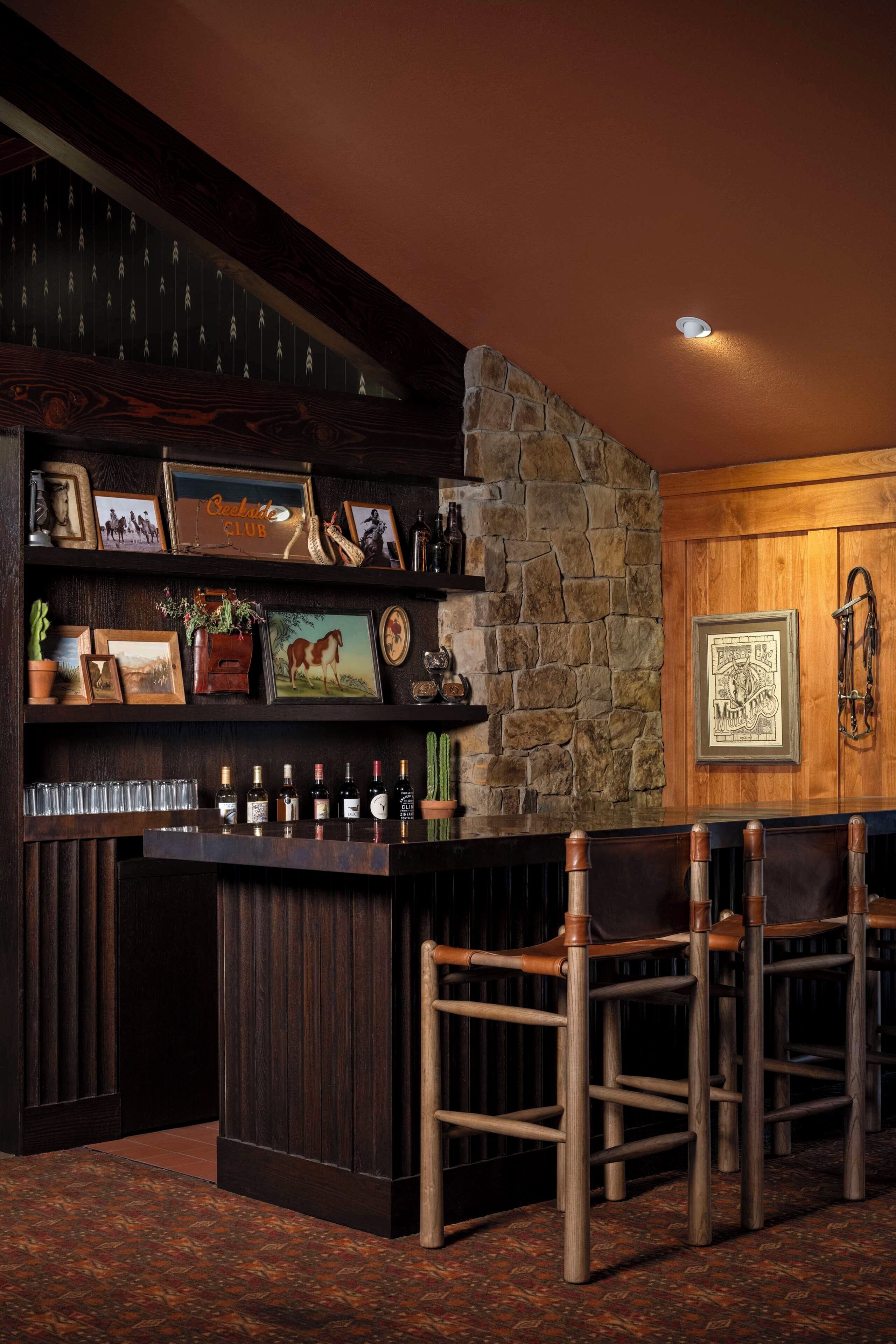 A bar area with a stone wall, wooden bar counter, and multiple framed pictures.
