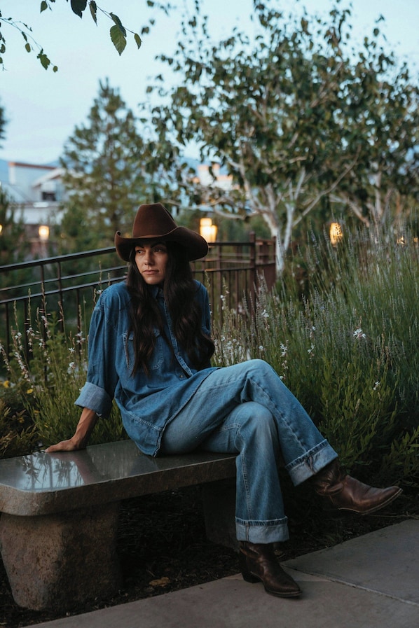 A person sitting on a bench outdoors with greenery and a fence in the background. - Wayfinder Bishop (Bishop)