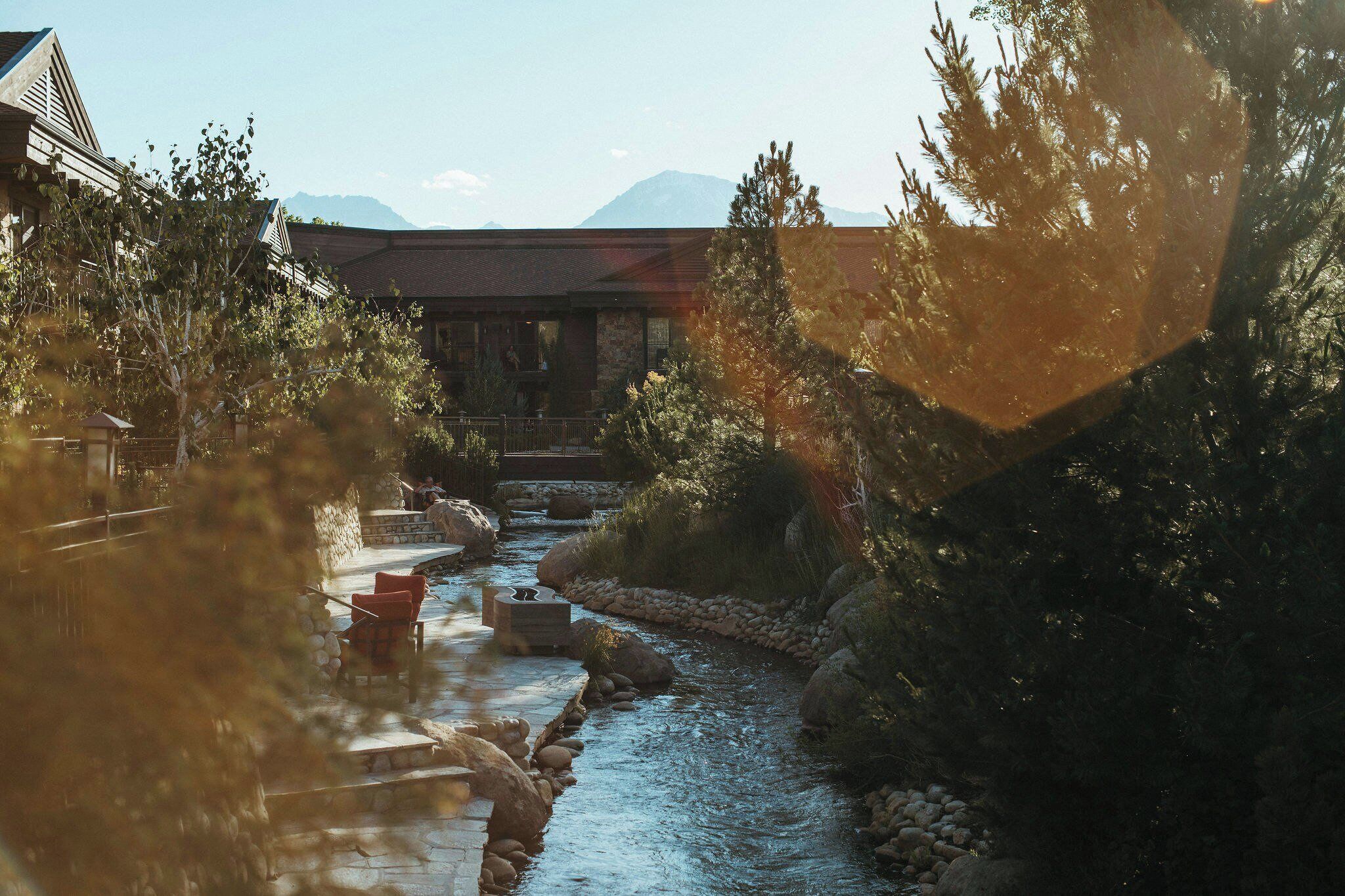 A river flowing through a landscaped area with a stone bridge, wooden deck, and seating.