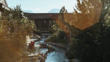 A river flowing through a landscaped area with a stone bridge, wooden deck, and seating.