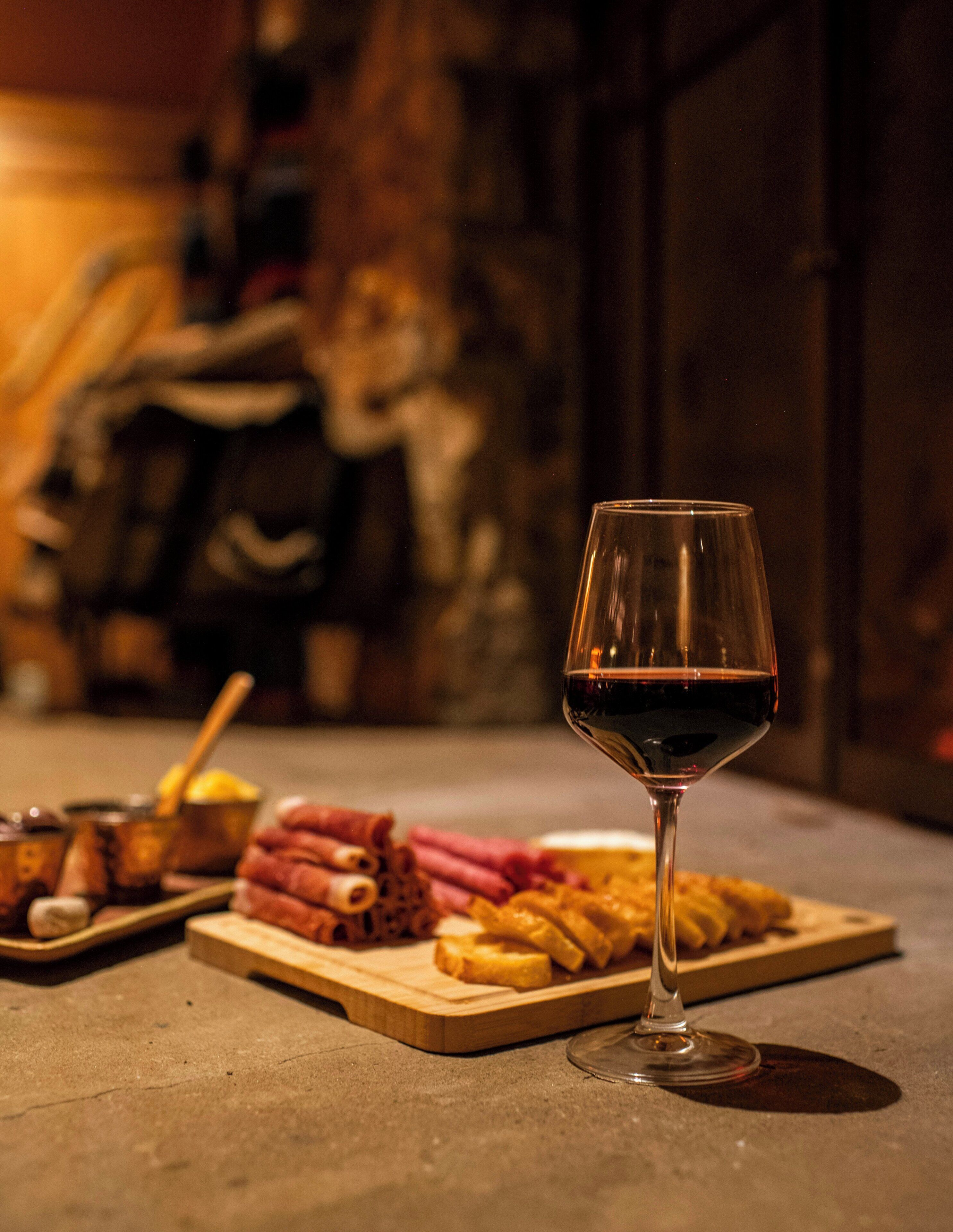 Una copa de vino tinto, una tabla de madera con diversos alimentos y un suelo de piedra.