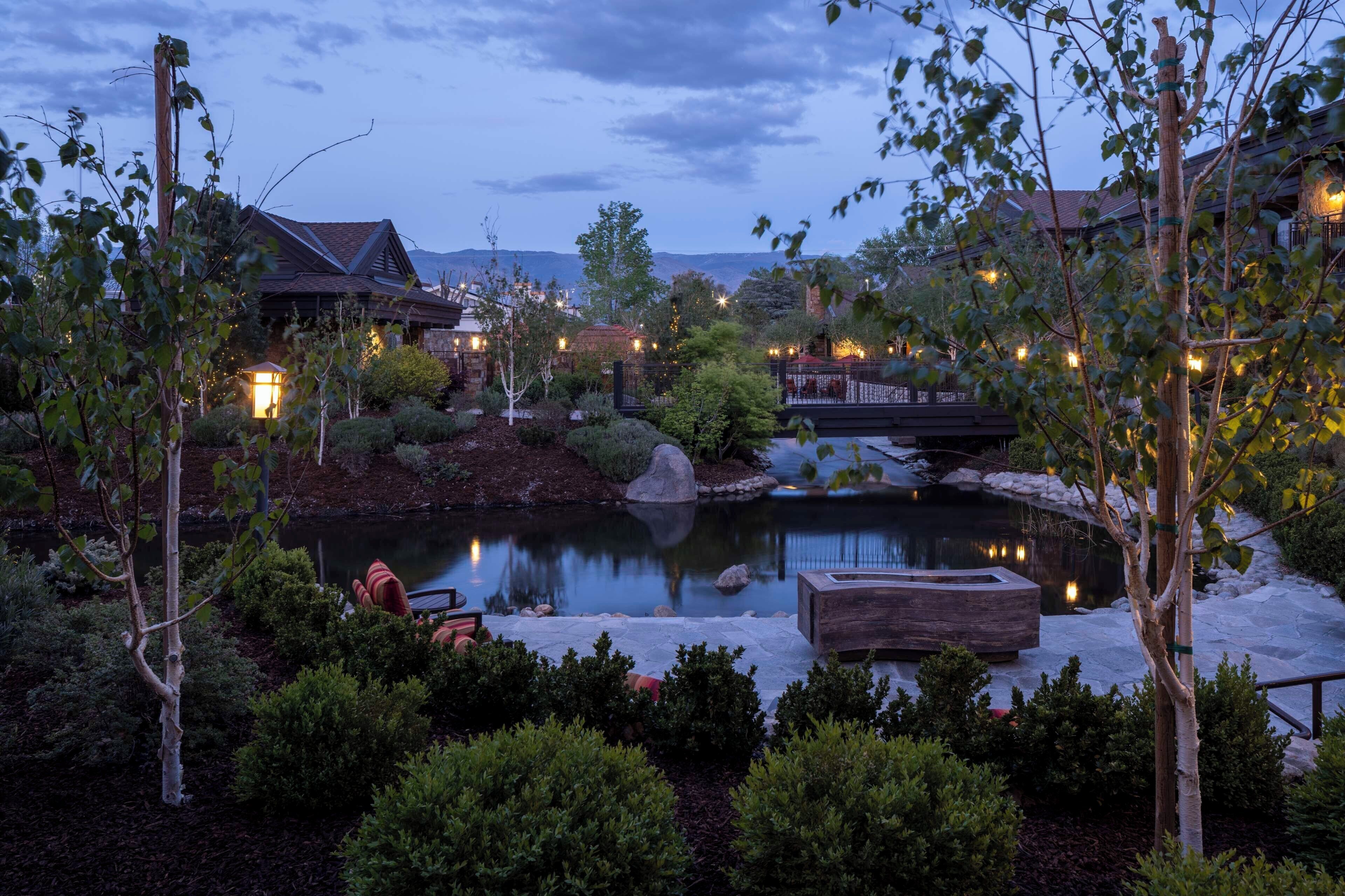 A serene outdoor setting with a pond, seating areas, and a bridge.