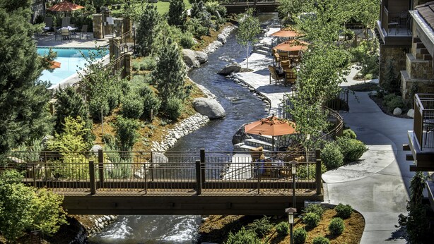 A river running through a landscaped area with a bridge, a pool, and outdoor seating areas. - Wayfinder Bishop (Bishop)