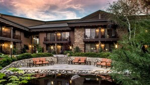 A two-story building with a stone facade, outdoor seating area with chairs, and a small pond. - Wayfinder Bishop (Bishop)