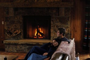 A room with a stone fireplace, a couch, and a glass of wine on a table. - Wayfinder Bishop (Bishop)