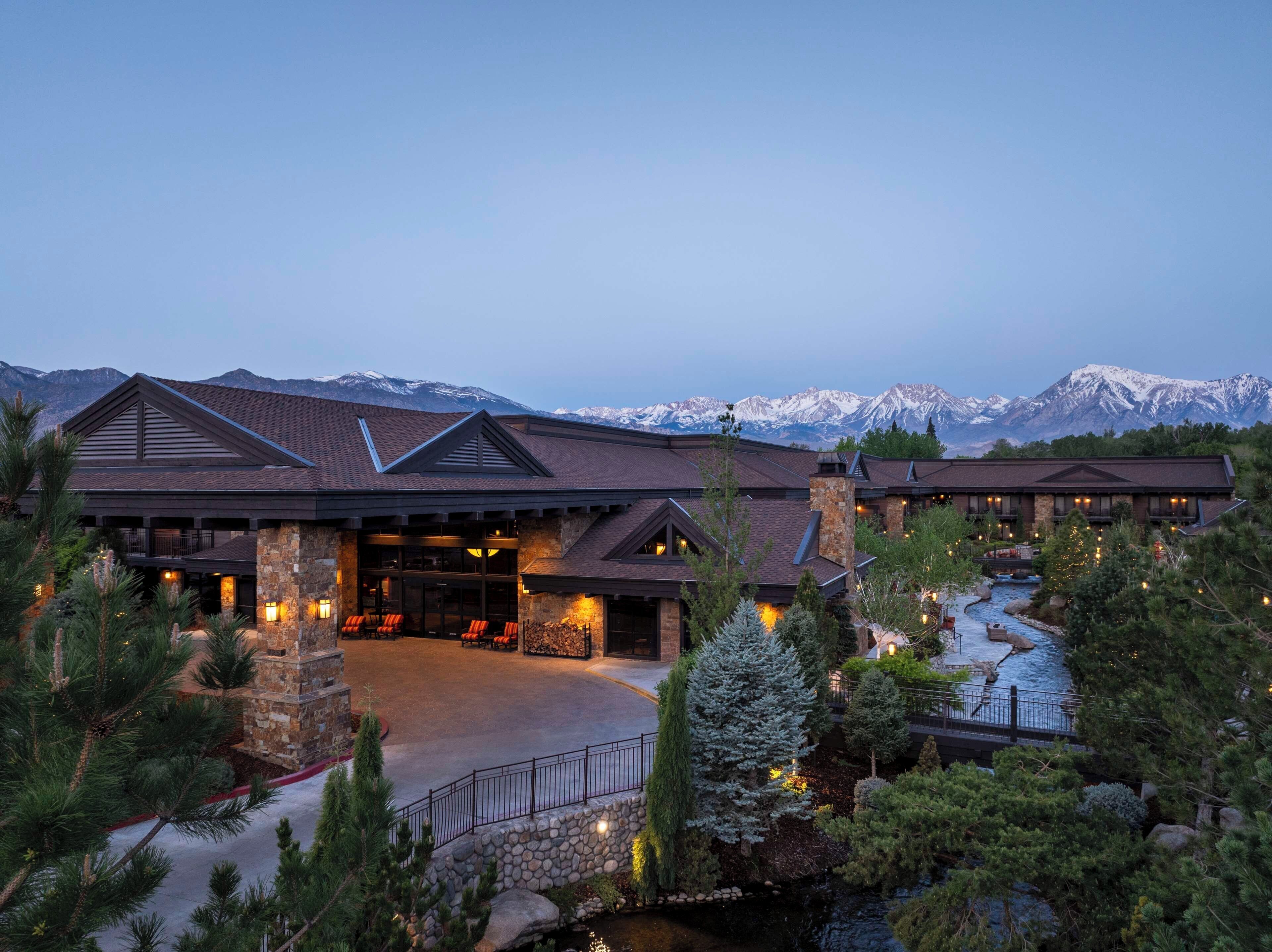 A lodge with a stone facade, a covered entrance, and a view of snow-capped mountains.