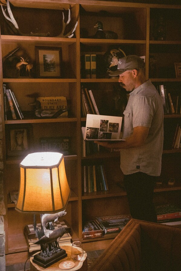 A man reading a book in a room with a bookshelf, a lamp, and a Scrabble game. - Wayfinder Bishop (Bishop)