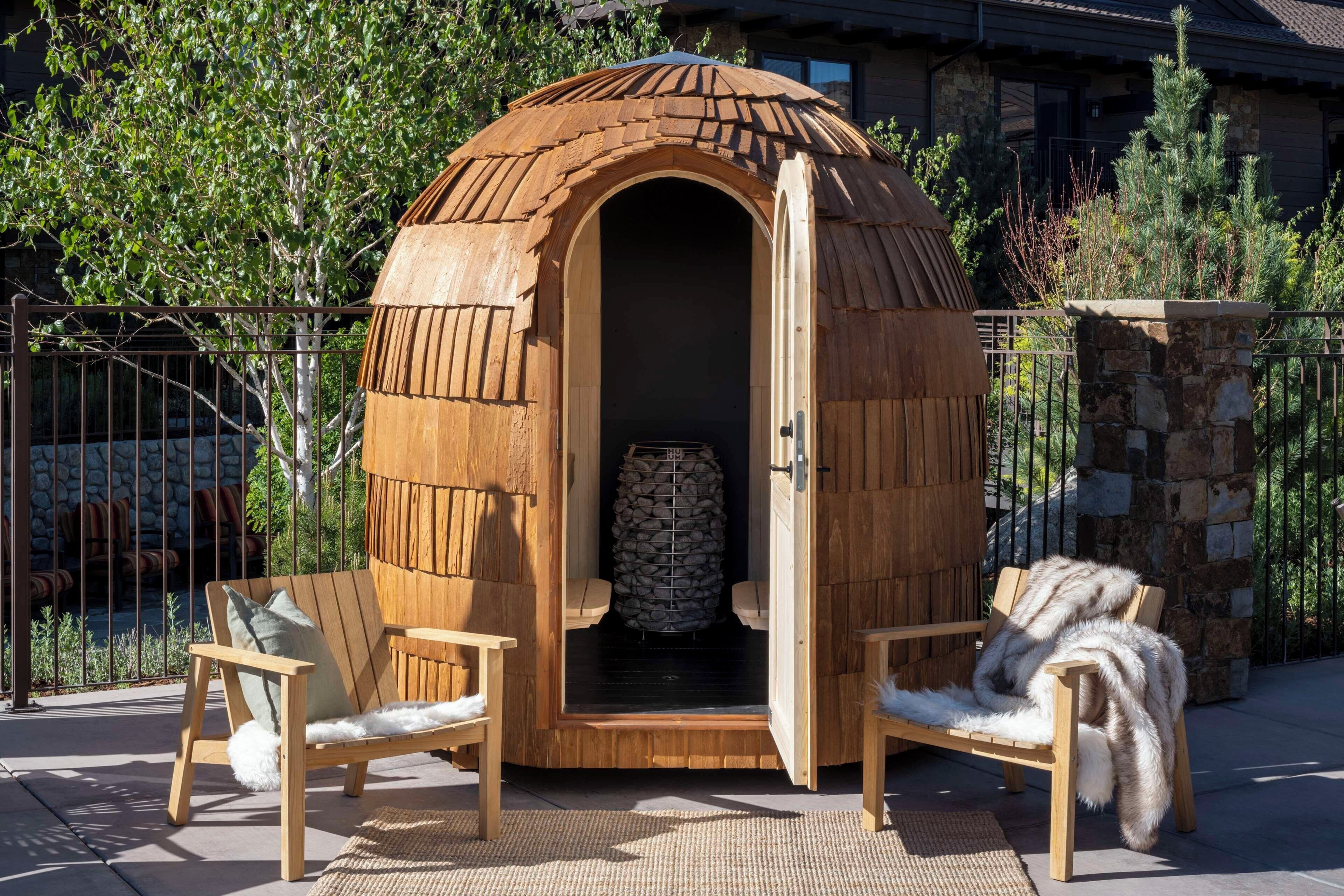 A wooden structure with an open door, a stone wall, and two chairs with fur throws.