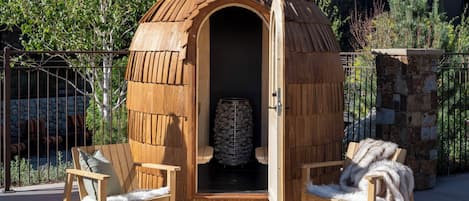 Una estructura de madera con puerta abierta, pared de piedra y dos sillas con mantas de piel.