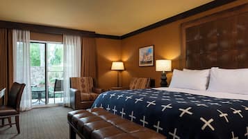 Habitación de hotel con una cama grande, dos sillas, un banco, una mesa y vistas a través de un ventanal.
