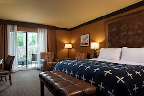 A hotel room with a large bed, two chairs, a bench, a table, and a view through a glass door. - Wayfinder Bishop (Bishop)