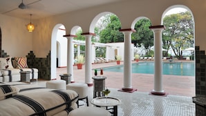 A poolside area with white columns, lounge chairs, and a pool. - The Victoria Falls Hotel (Victoria Falls)