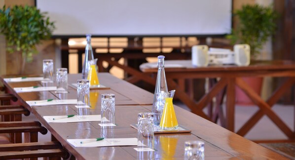 A conference table with clear glassware, documents, and pens, set in a room with a projector screen and wooden furniture. - The Victoria Falls Hotel (Victoria Falls)