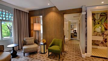 A hotel room with a patterned carpet, a green armchair, a beige armchair, a small round table, and a lamp.