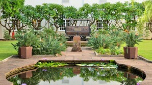 A serene garden with a pond, benches, and lush greenery. - The Victoria Falls Hotel (Victoria Falls)