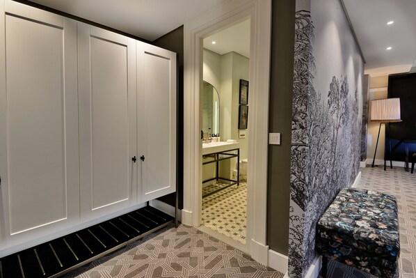 A hallway with a patterned floor, a white wardrobe, a bench, and a wall with a black and white mural. - The Victoria Falls Hotel (Victoria Falls)